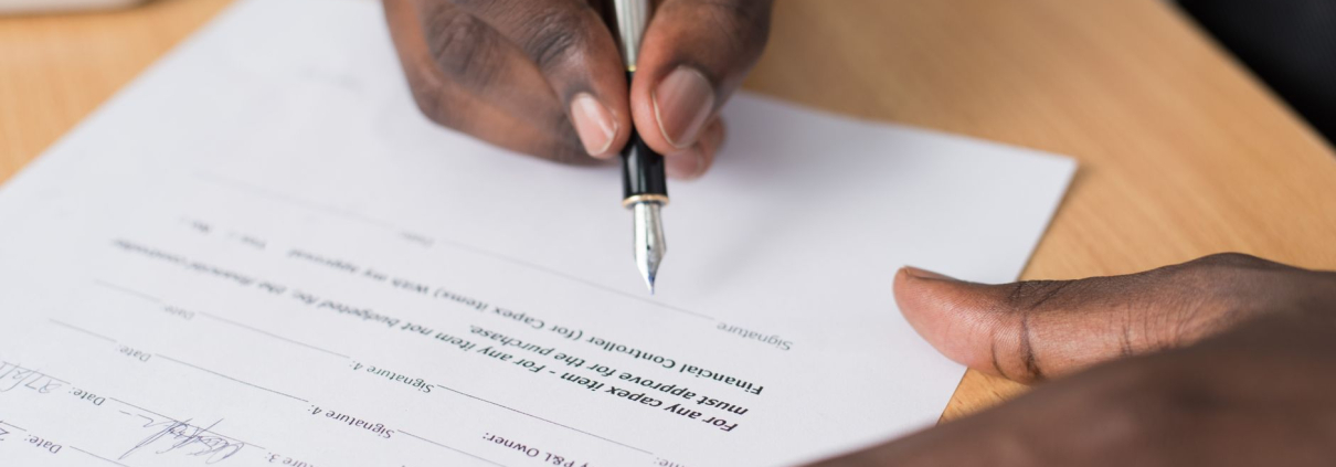 Manos firmando un documento con bolígrafo sobre mesa de madera