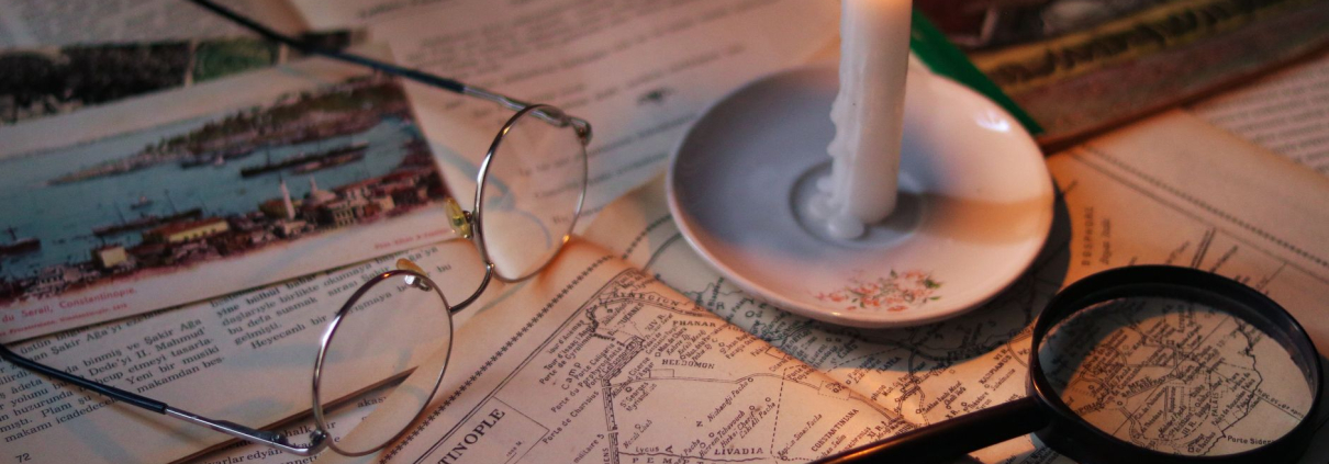 Documentos antiguos con mapas, gafas, lupa y vela encendida sobre mesa de madera para ilustrar investigación documental