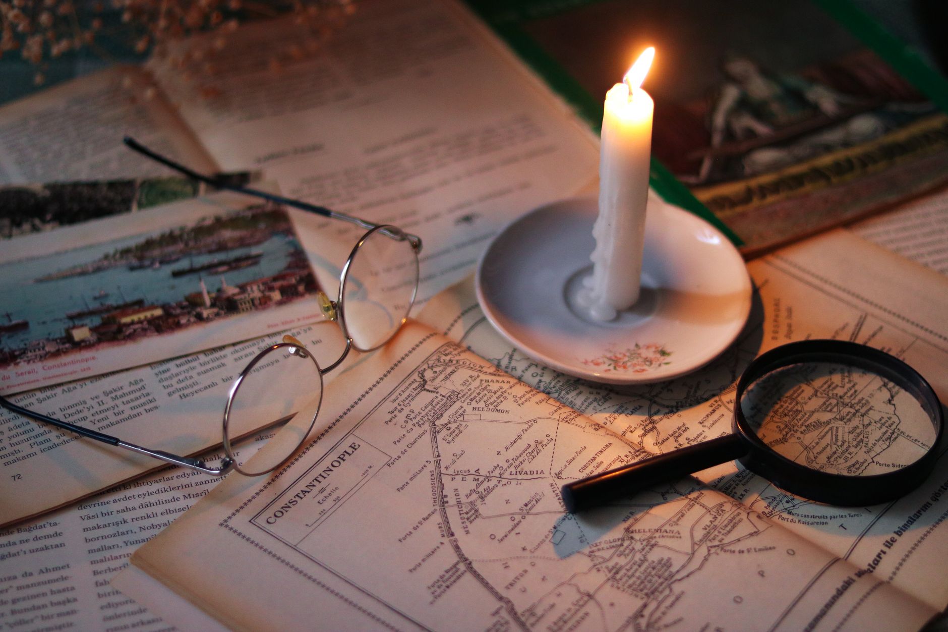 Documentos antiguos con mapas, gafas, lupa y vela encendida sobre mesa de madera para ilustrar investigación documental